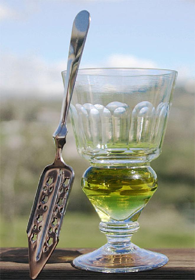 Una copa de absenta con su color natural (antes de la adición del agua) y una cuchara típica.