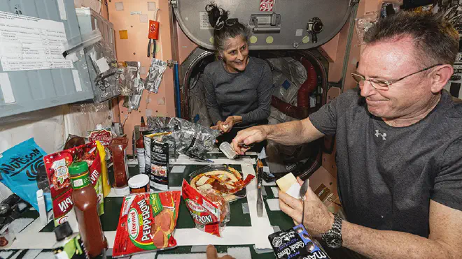 Suni Williams, la comandante de la Estación Espacial observa a Butch Wilmore mientras prepara pizza. Ambos llegaron a bordo de Starliner, y regresarán en febrero de 2025 a bordo de SpaceX Dragon-9