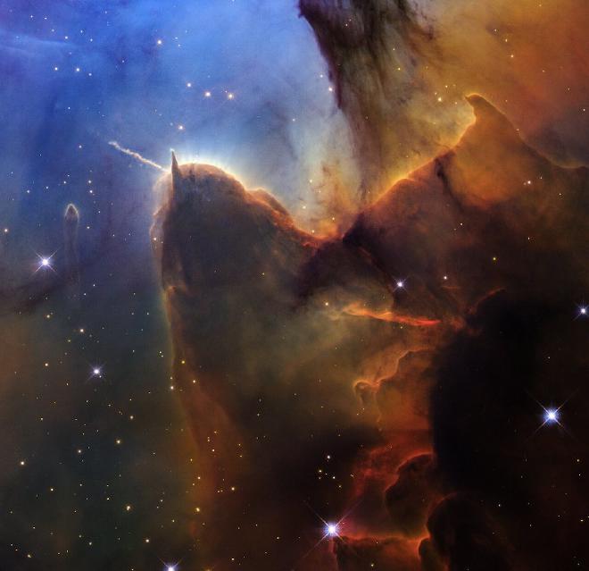 El Hubble nos fascina con una vista recortada de una vasta región de formación estelar conocida como la Nebulosa Trífida. La parte superior izquierda es de un azul brillante. Los colores marrón y ámbar van desde la parte superior derecha hasta el centro en líneas irregulares y superpuestas hasta la parte inferior central. En la esquina inferior derecha, la vista es casi negra. Pequeñas estrellas de color ámbar aparecen a lo largo de la escena. Hacia la izquierda hay una figura marrón prominente que parece una cabeza con dos cuernos. El cuerno izquierdo apunta hacia la izquierda y es ondulado. El cuerno derecho es triangular y apunta hacia arriba. El polvo marrón continúa, fluyendo hacia abajo, como si recorriera un respaldo, y subiendo hacia la parte superior derecha. Una línea prominente, de aproximadamente la misma longitud que el cuerno izquierdo, aparece debajo del centro del cuerpo y cambia de naranja a rojo. Un pequeño pilar semitransparente separado está a la izquierda de la cabeza. Aparecen en la mitad inferior unas pocas estrellas azules de primer plano ligeramente más grandes con cuatro picos de difracción. Crédito de la imagen: NASA, ESA, STScI. Image processing: J. DePasquale (STScI)