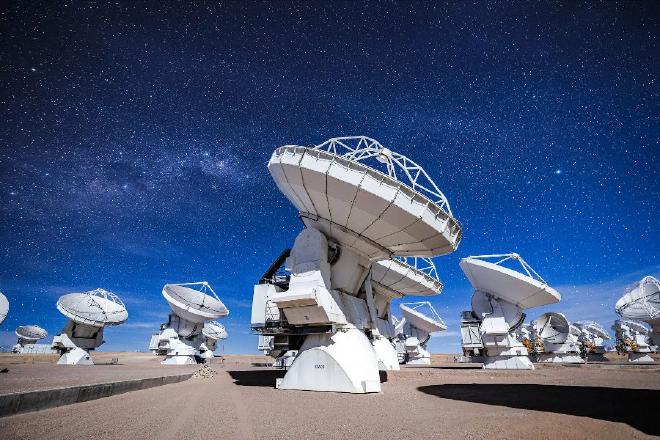 Antena DV-59 de ALMA en primer plano, con otras antenas observando el cielo en una noche dominada por la Luna. Crédito de la imagen: ALMA/Alex Pérez / CC BY 4.0