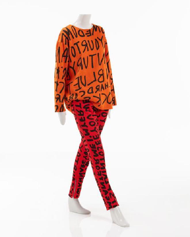 Camisa y pantalón de color naranja fluorescente muy llamativo, con el estampado de grafiti característico de Stephen Sprouse. Crédito de la imagen: Museo de Arte de Indianápolis en Newfields, Fondo de Adquisición de la Sociedad de Artes de la Moda, Fondo de Adquisición Joanne Sprouse, adquirido con fondos proporcionados por Penny Rosenthal, 2021.187.