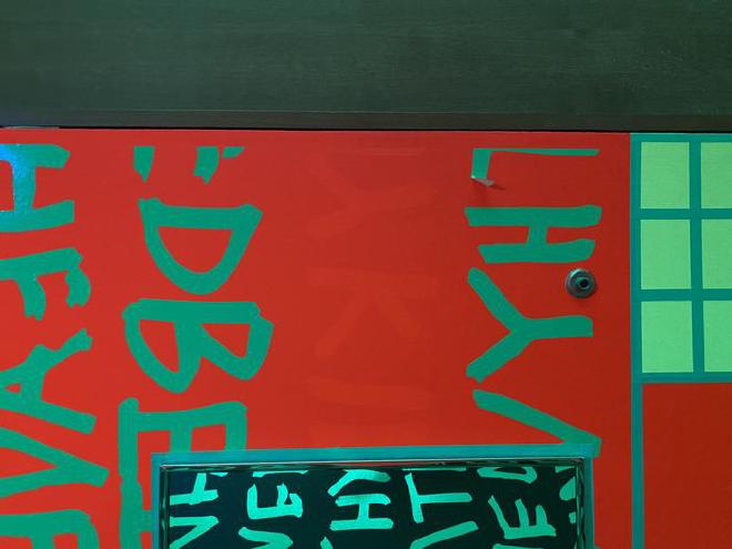 Primer plano de un mural fluorescente en Newfields que muestra pintura roja DayGlo brillante en un área que antes estaba protegida de la luz por las letras de vinilo verde. Crédito de la imagen: Amanda Holden / Museo de Arte de Indianápolis en Newfields