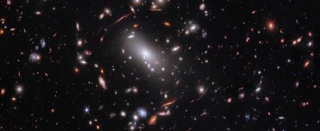 Miles de galaxias brillantes están unidas entre sí por su gravedad y forman un cúmulo masivo clasificado formalmente como MACS J1423. El óvalo blanco brillante más grande es una galaxia elíptica supergigante que es el miembro dominante de este cúmulo de galaxias. El cúmulo de galaxias actúa como una lente, magnificando y distorsionando la luz de los objetos que se encuentran por detrás de él, un efecto conocido como lente gravitacional que tiene grandes beneficios para la investigación. Los astrónomos pueden estudiar las galaxias con efecto lente en detalle, como la galaxia Firefly Sparkle. Esta imagen de 2023 es de la NIRCam (cámara de infrarrojo cercano) del telescopio espacial James Webb. Los investigadores utilizaron Webb para estudiar el mismo campo que el telescopio espacial Hubble fotografió en 2010. Gracias a su especialización en imágenes de infrarrojo cercano de alta resolución, Webb pudo mostrar a los investigadores muchas más galaxias con más detalle. Crédito: NASA, ESA, CSA, STScI, C. Willott (NRC-Canada), L. Mowla (Wellesley College), K. Iyer (Columbia)