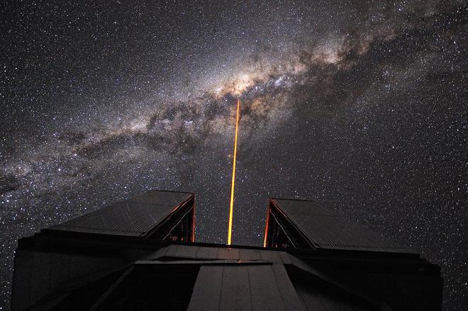 El Laser Guide Star (LGS) es lanzado desde el Telescopio VLT Yepun de 8.2 metros, apuntando al centro de nuestra galaxia, en el corazón de la parte más brillante de la Vía Láctea. El rayo láser es parte del sistema de óptica adaptativa. Crea una estrella artificial a 90 kilómetros de altitud en la mesosfera de la Tierra. Esta estrella es utilizada como referencia para corregir imágenes y espectros de la distorsión provocada por la atmósfera. El plano de la Vía Láctea es cruzado por prominentes surcos negros, grandes nubes interestelares de polvo que bloquea la luz visible. Gracias a los instrumentos infrarrojos montados en el Telescopio Yepun, los astrónomos pueden ver a través de estas nubes y estudiar el complejo y turbulento corazón de nuestra galaxia, donde un agujero negro supermasivo esta al acecho. El Very Large Telescope esta compuesto de cuatro Unidades de Telescopios de 8.2 metros (UT, donde Yepun es el UT4) sumado a los cuatro Telescopios Auxiliares d 1.8 metros. Crédito: G. Hüdepohl (atacamaphoto.com)/ESO