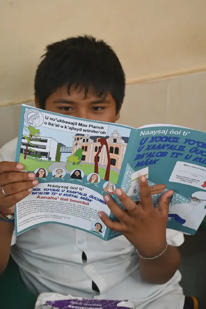 Un poblador joven de Tixcacaltuyub lee uno de los libros en idioma yucateco para colorear que Warinner y Barquera hicieron sobre la ciencia arqueológica